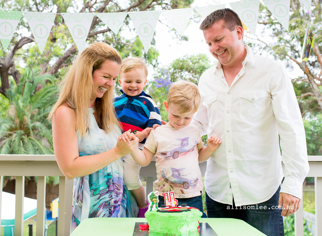 Four year old blowing out candles on birthday cake with mum and dad